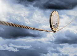 Imagen que representa una moneda de 1 euro rodando por una cuerda tensa con nubes de tormenta en el fondo